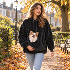 Woman on an autumn walk in a UK park wearing the black CuddleCarry pouch hoodie with a small dog in the front pouch
